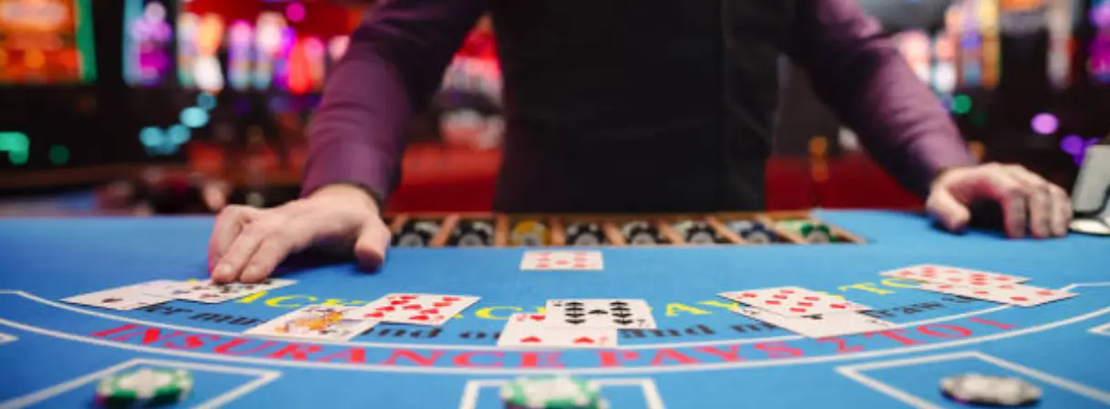A casino dealer in a purple shirt is arranging playing cards on a vibrant blue blackjack table.