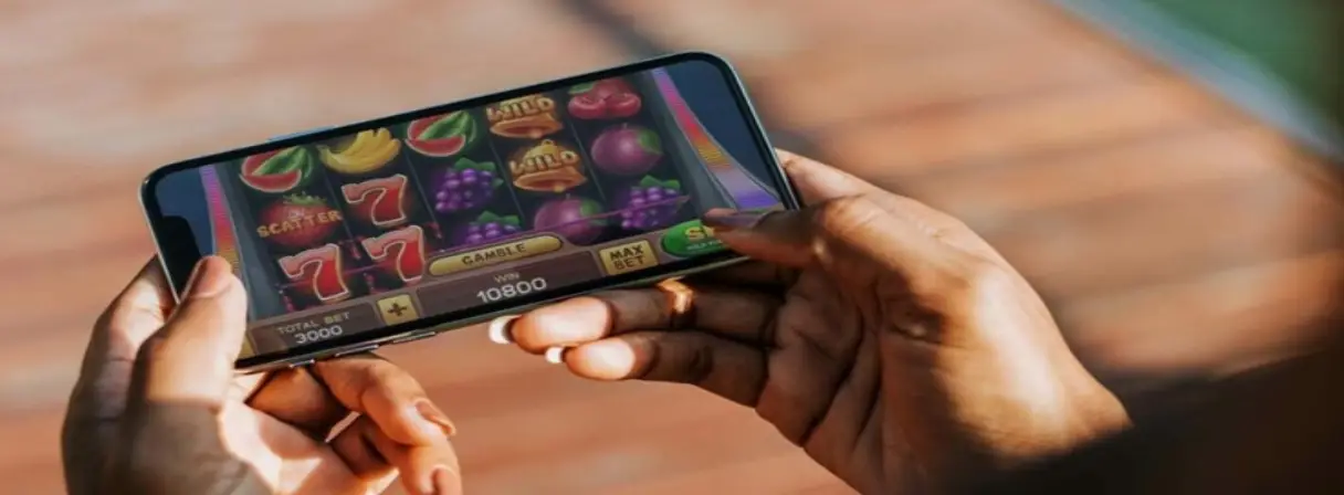 Person holding a smartphone displaying a colorful casino slot game with symbols like fruit