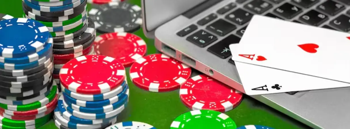 Poker chips in various colors are stacked near a laptop on a green table